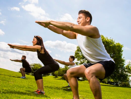 Group of people doing squats on a sunny grassy hill in a park.
