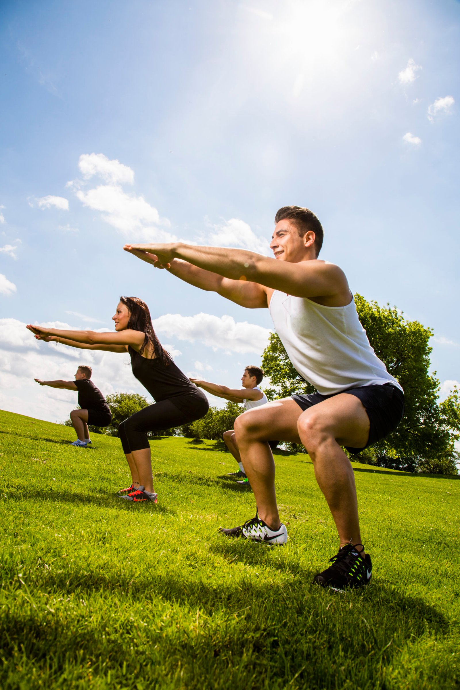 Outdoor Hybrid Training Bootcamp klas - ThriveLab Group of people doing squats on a sunny grassy hill in a park.